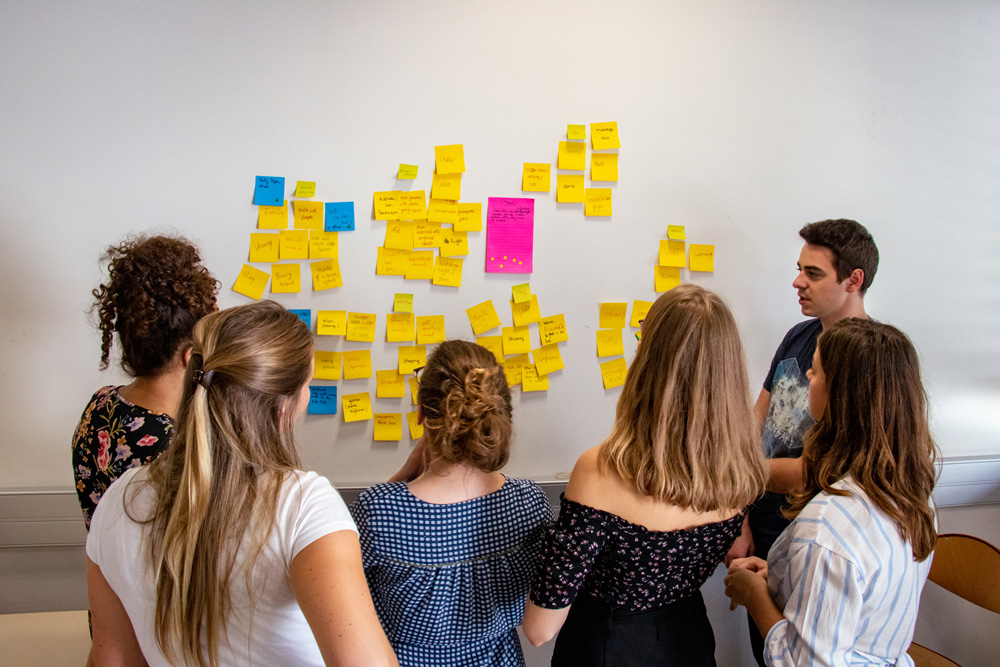 Photos d'un groupe d'étudiants en brainstorming pour un projet devant un mur de post-it d'idées - BUT GACO MMI PEC